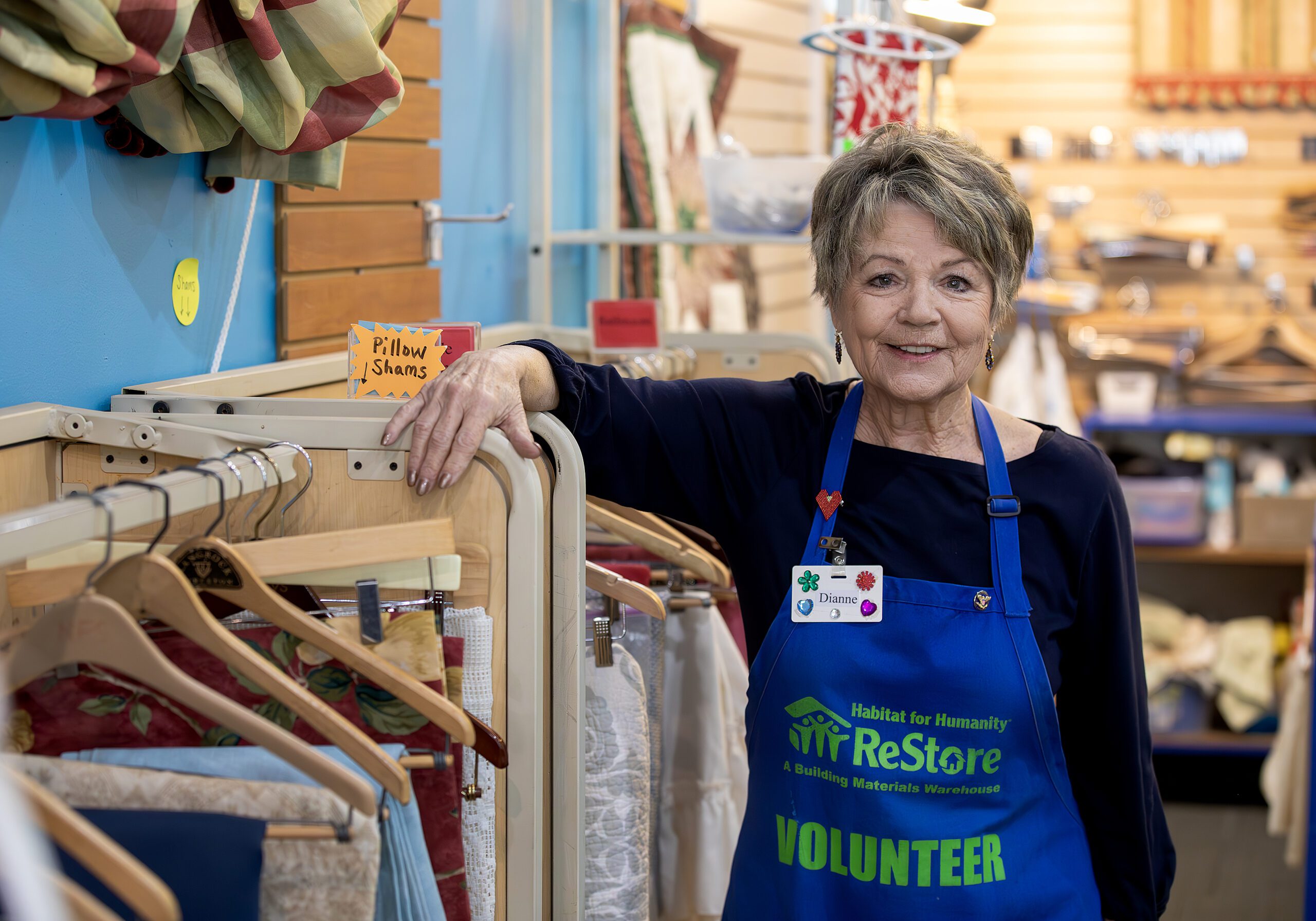 Dianne Colton volunteering at Habitat ReStore, standing near linens section.