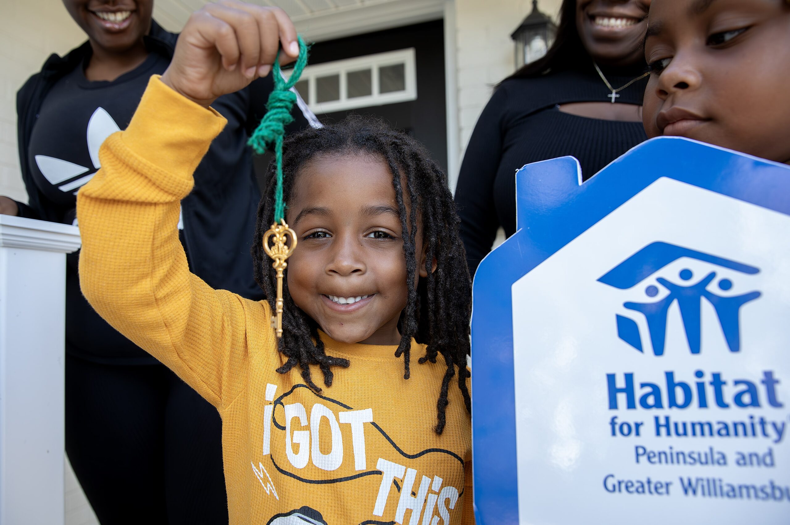 Smiling child holding a key in front of a Habitat for Humanity home