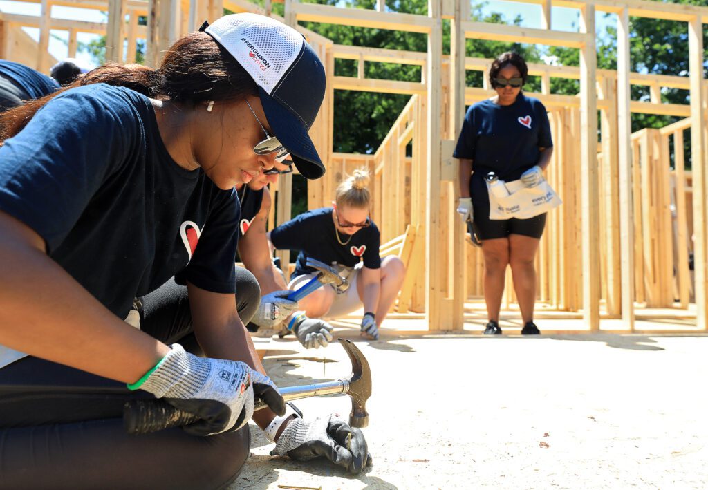 Volunteers hammer wood panels into home framing.