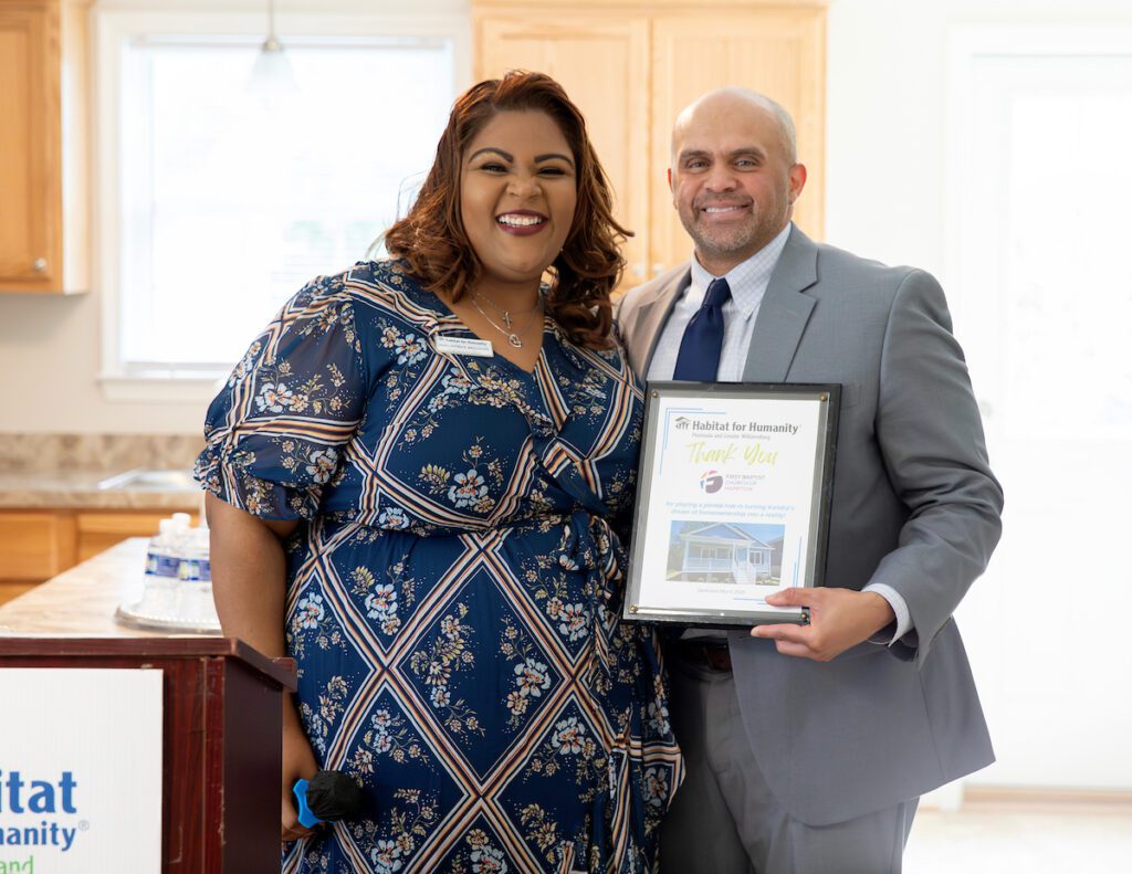 Habitat CEO Shauntrice Williams and a First Baptist Church representative hold a framed certificate during the dedication ceremony.