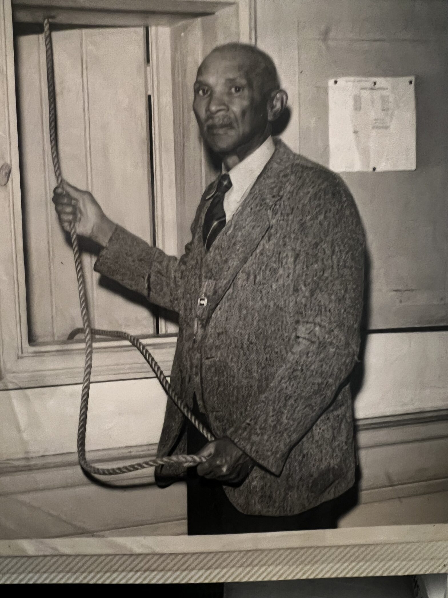 A dignified portrait of Henry Billups holding the Wren bell rope