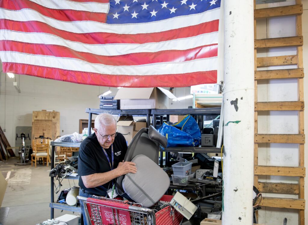 Tim McSwain holding an upcycled car seat in the ReStore warehouse.
