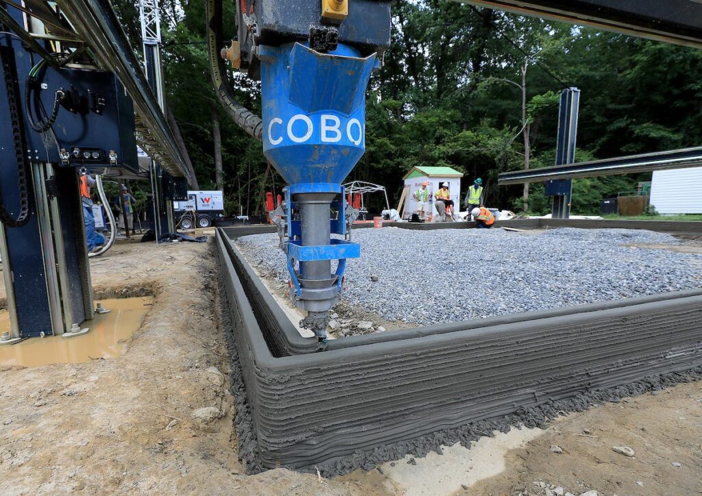 The printer head of a giant 3D printer begins laying down layers of cement for the foundation of a Habitat for Humanity home in Williamsburg