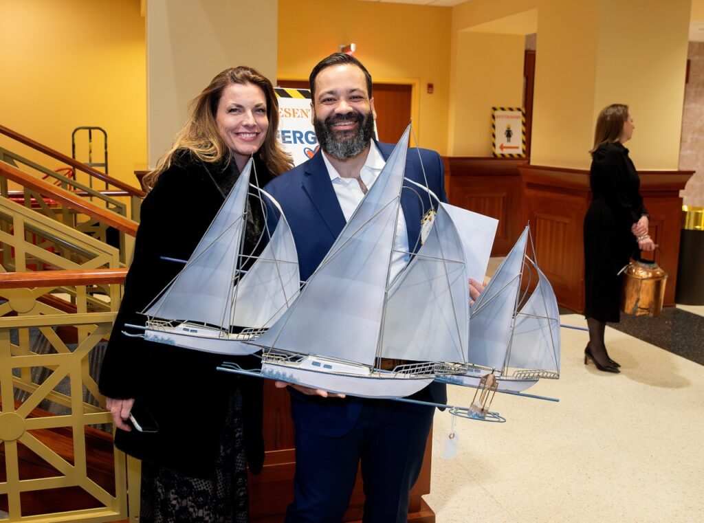 Two people posing with sailboat sculpture. 
