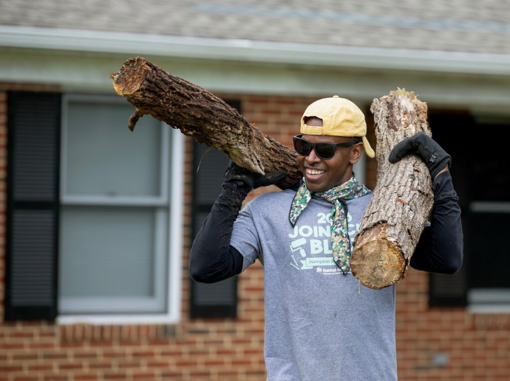Man holding log in front of house