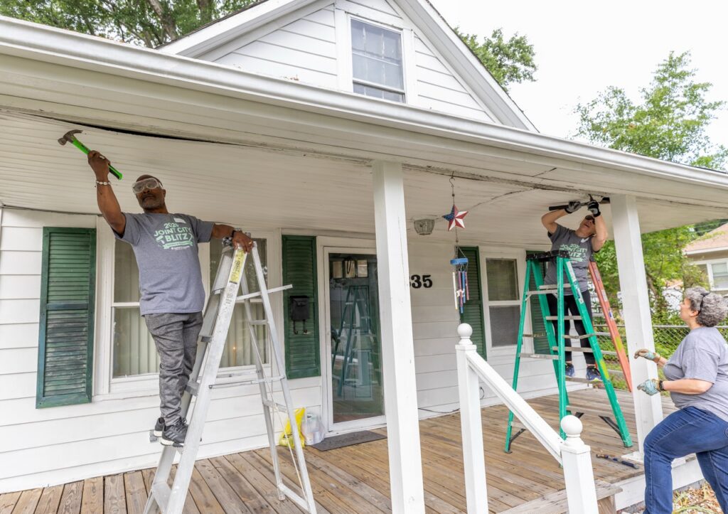 People hammering and on a ladder and working on a white house