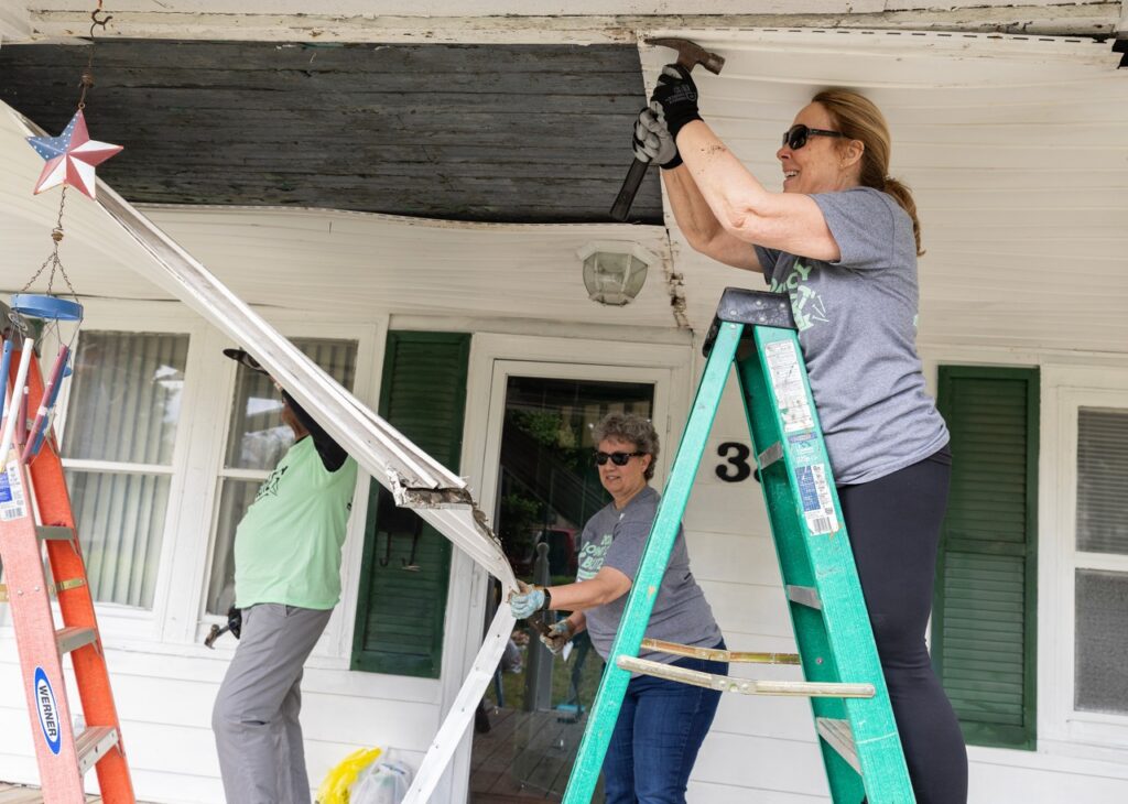 People hammering and on a ladder and working on a white house