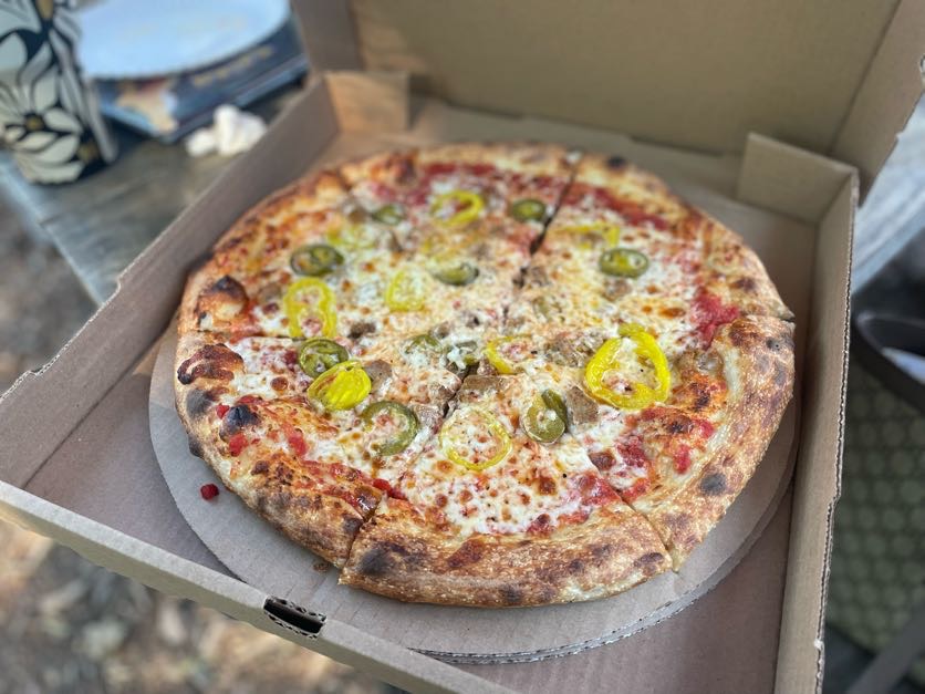 Pizza with jalapeños and banana peppers in an open box on a table, ready to eat outdoors.