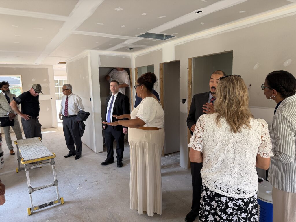 A group of people standing together in a Habitat construction house, engaged in conversation and smiling at each other.