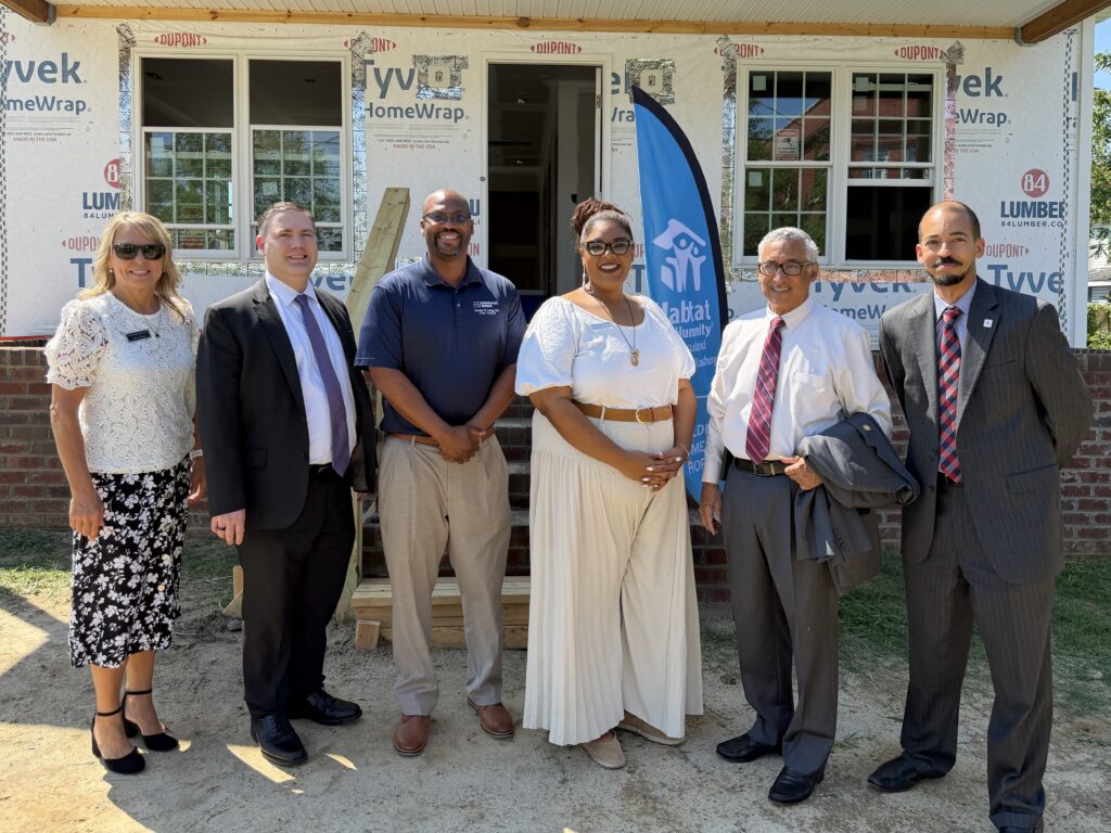 A diverse group of people smiling and standing together in front of a house, showcasing community and togetherness.