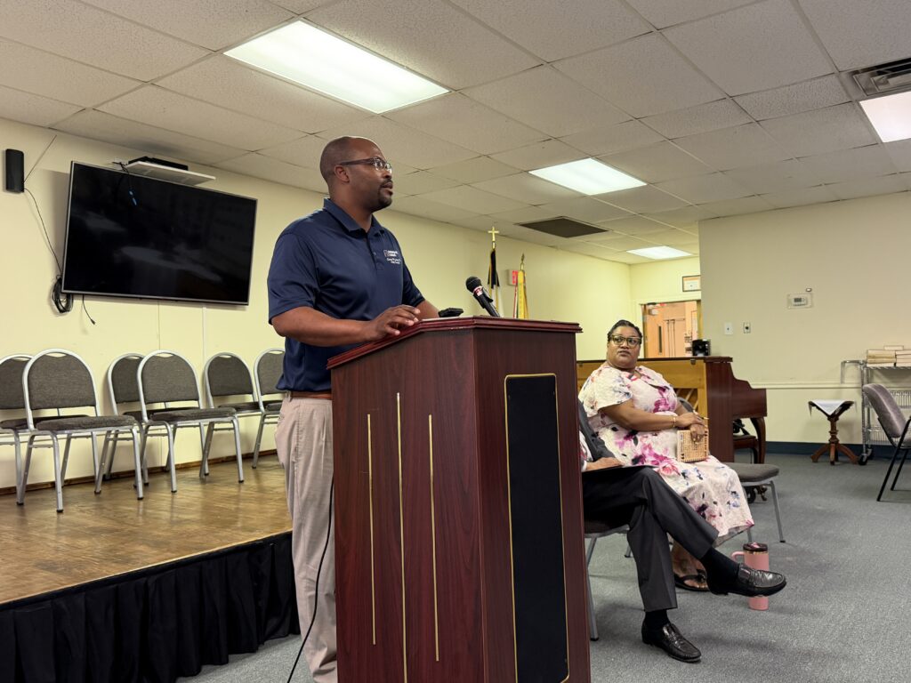 Councilman Long speaks at a podium, addressing an audience of engaged listeners in a conference setting.