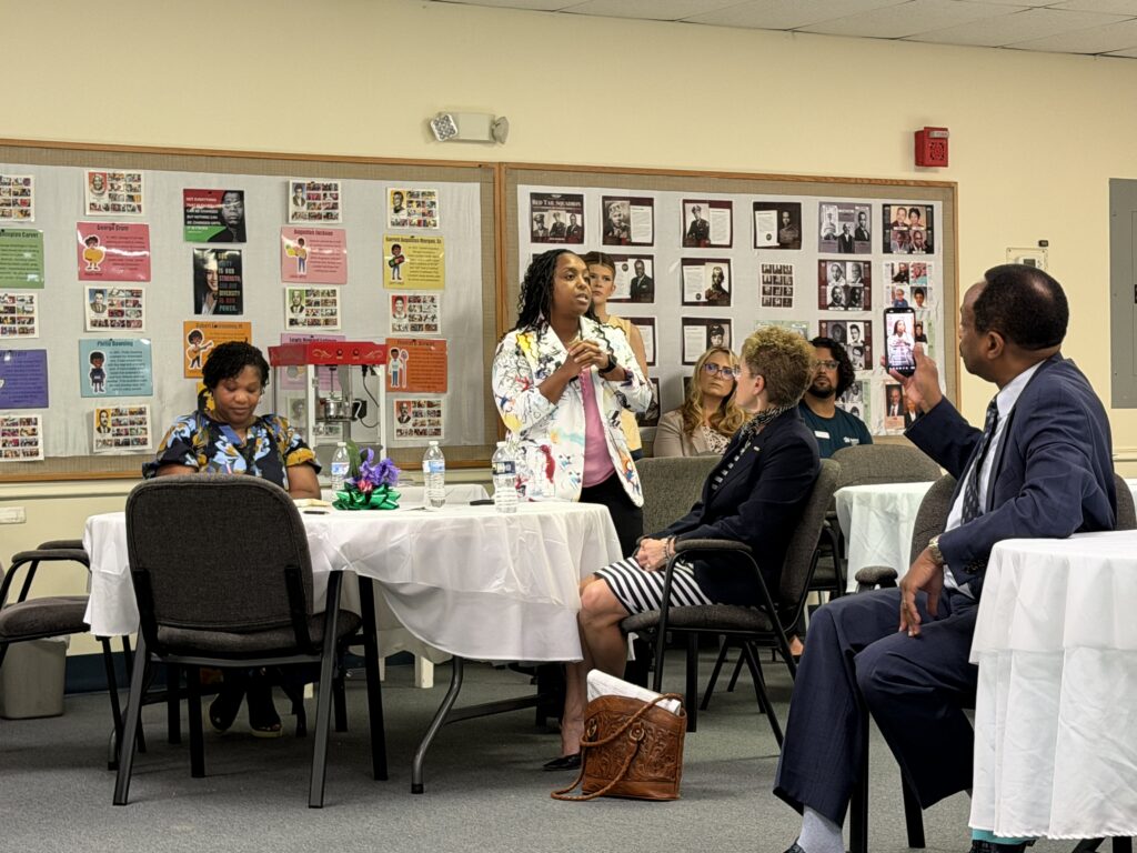 Charvālla West stands confidently at a podium, presenting to an engaged audience of diverse individuals.