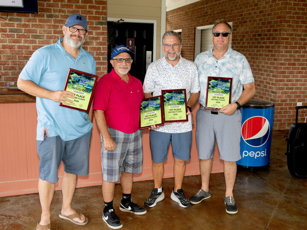 Four men standing indoors, each holding a plaque, smiling at the camera near a Pepsi-branded trash can.